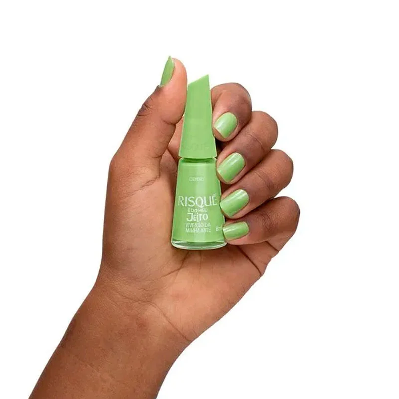 Mão segurando esmalte Risqué verde cremoso mostrando cobertura e acabamento