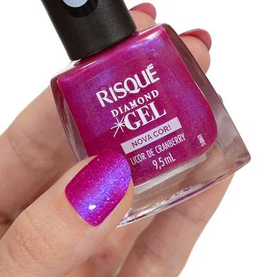 Mão com unhas pintadas na cor Licor de Cranberry Metálico segurando o frasco